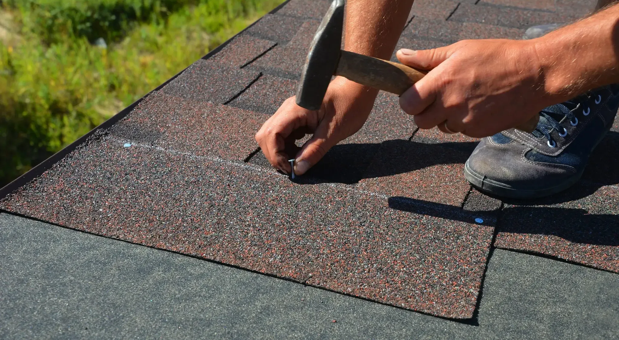 A roofer nailing down asphalt shingles during a roof installation